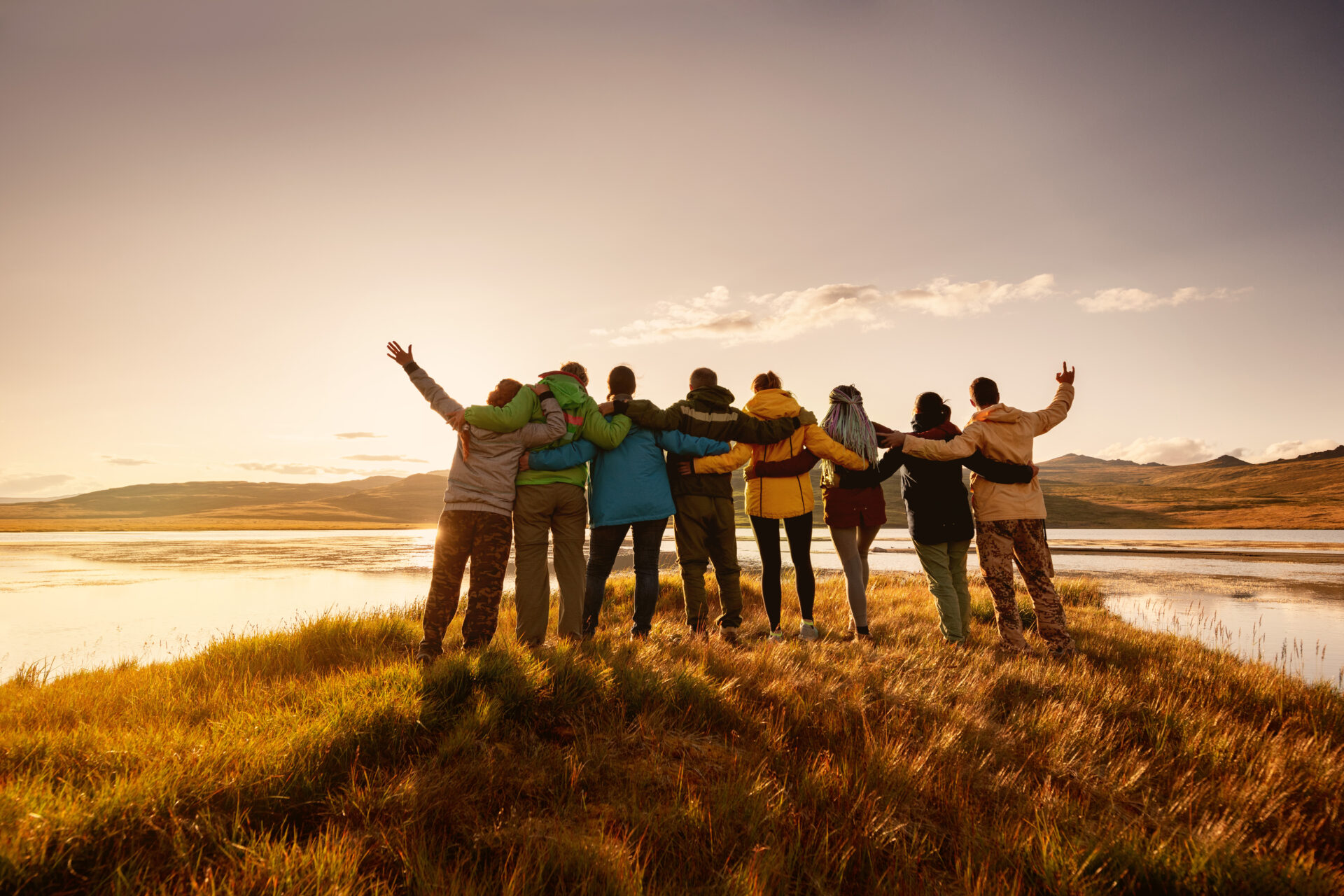 Big happy family is standing and hugging together against lake in mountains and sunset sky